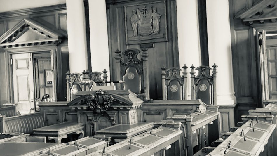 A grayscale photo of South Shields Town Hall Chamber, empty and looking towards the high chairs that tower over the chamber. 